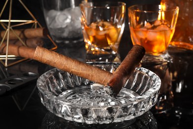 Photo of Smoldering cigars, ashtray and whiskey on black mirror surface, closeup