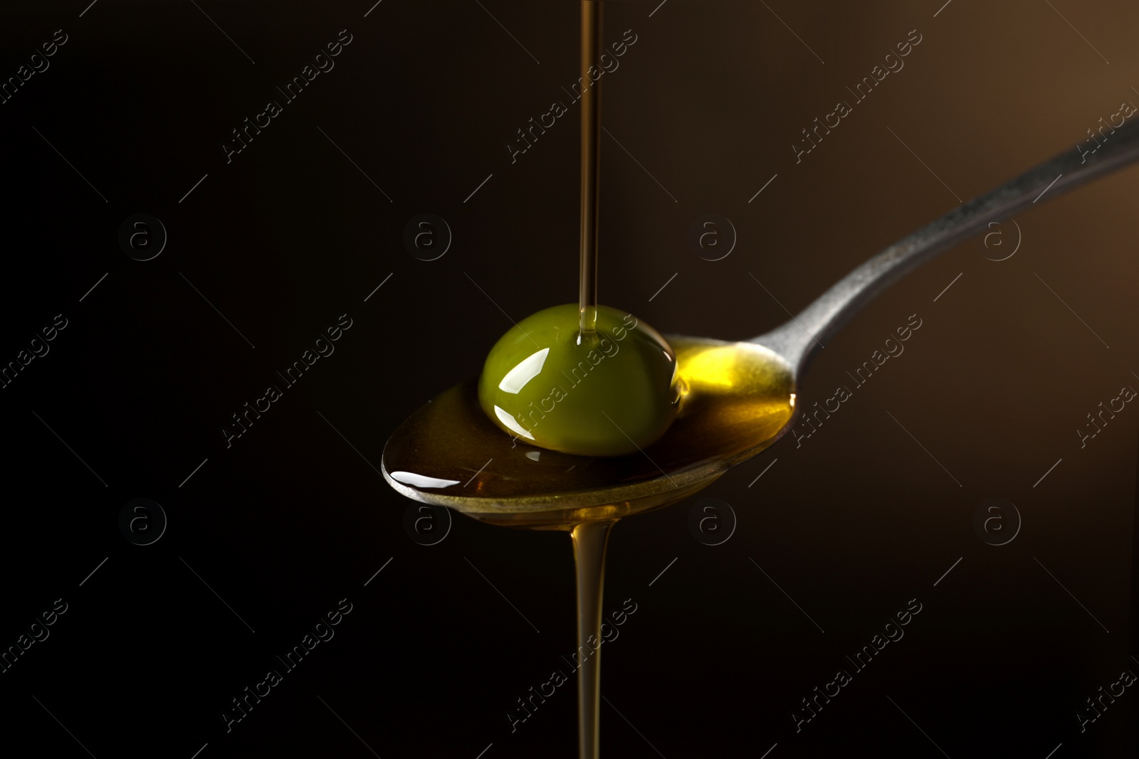 Photo of Pouring oil into spoon with ripe olive against dark background, closeup