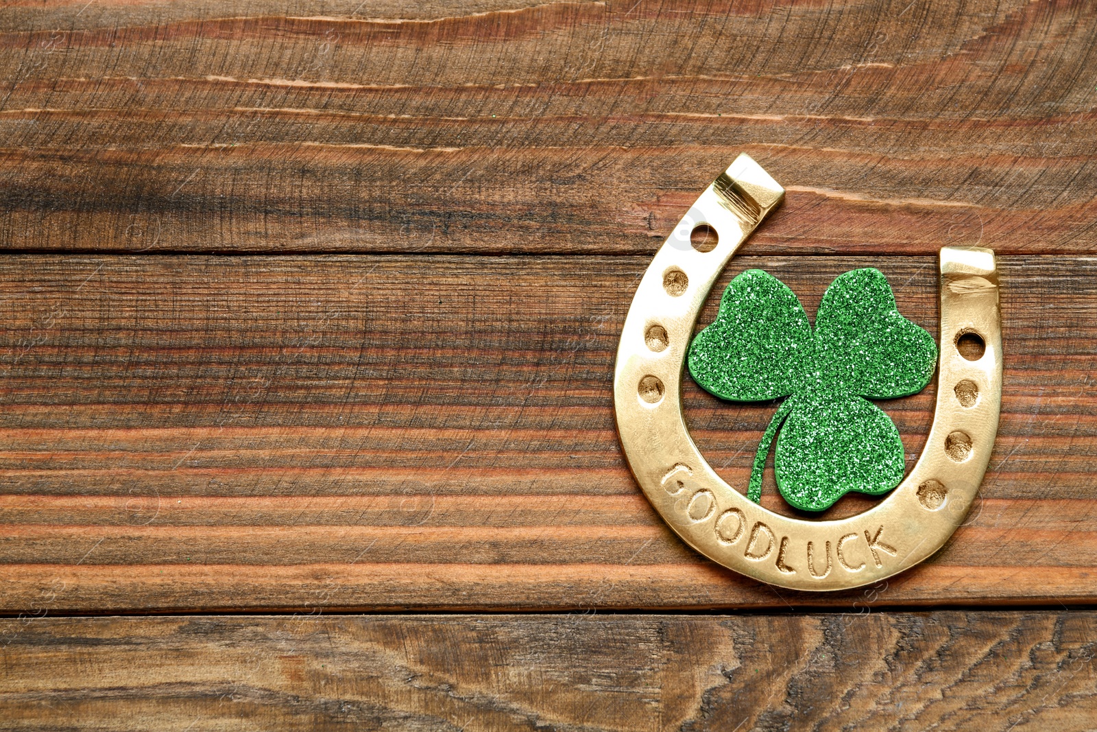 Photo of Golden horseshoe and decorative clover leaf on wooden table, flat lay with space for text. Saint Patrick's Day celebration