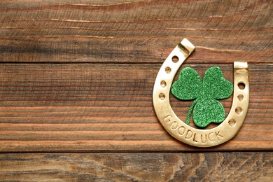 Photo of Golden horseshoe and decorative clover leaf on wooden table, flat lay with space for text. Saint Patrick's Day celebration