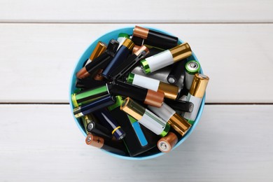 Image of Used batteries in bucket on white wooden table, top view