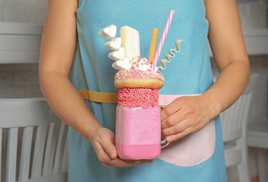 Woman holding mason jar of tasty milk shake with sweets indoors, closeup
