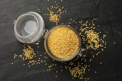 Millet groats in glass jar on black table, top view