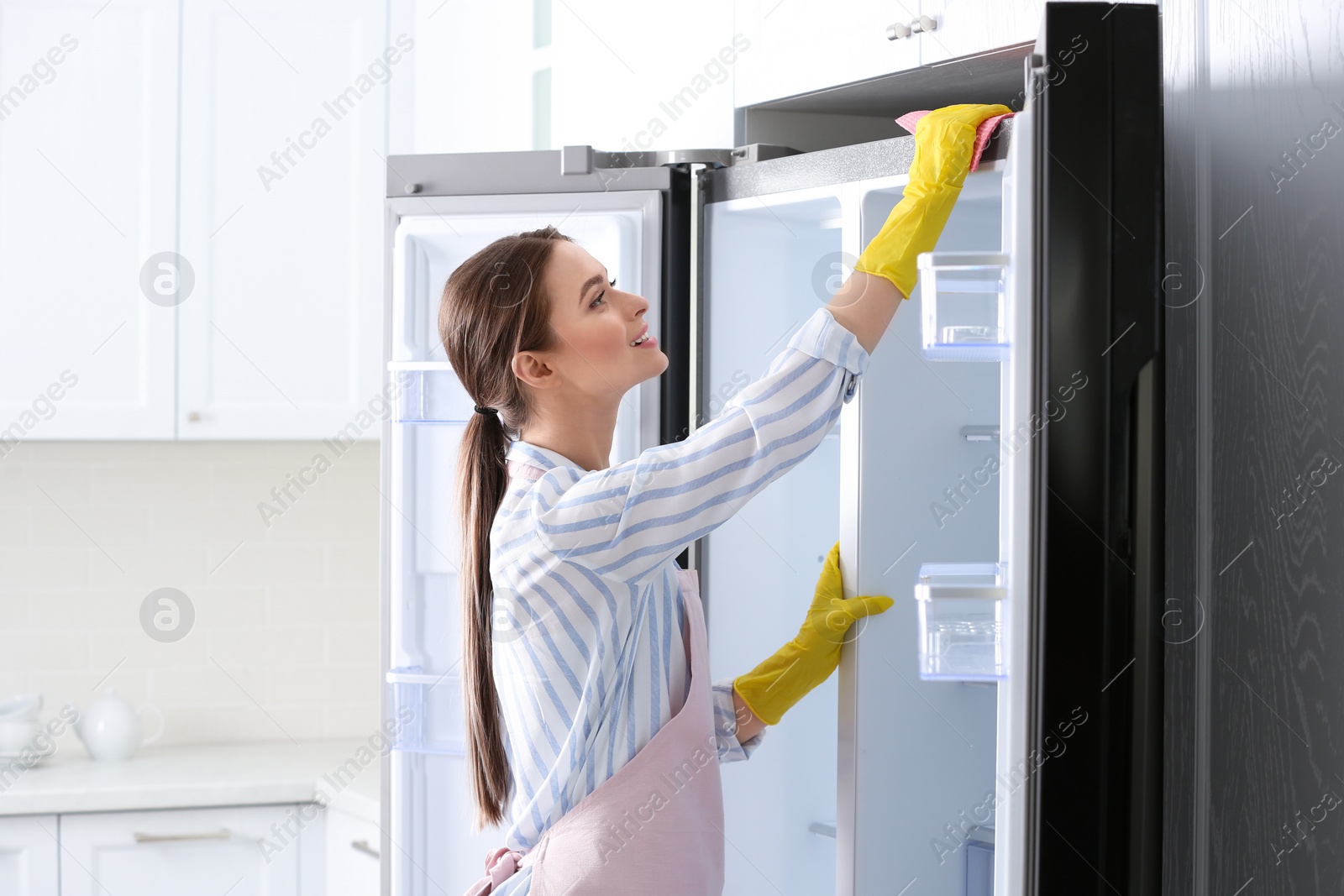 Photo of Woman in rubber gloves cleaning refrigerator at home