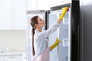 Woman in rubber gloves cleaning refrigerator at home