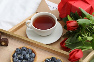 Photo of Tasty breakfast served in bed. Delicious tartlets, tea, flowers and card with phrase Love You on tray