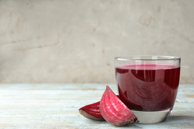 Cut beet and glass of juice on wooden table against grey background. Space for text