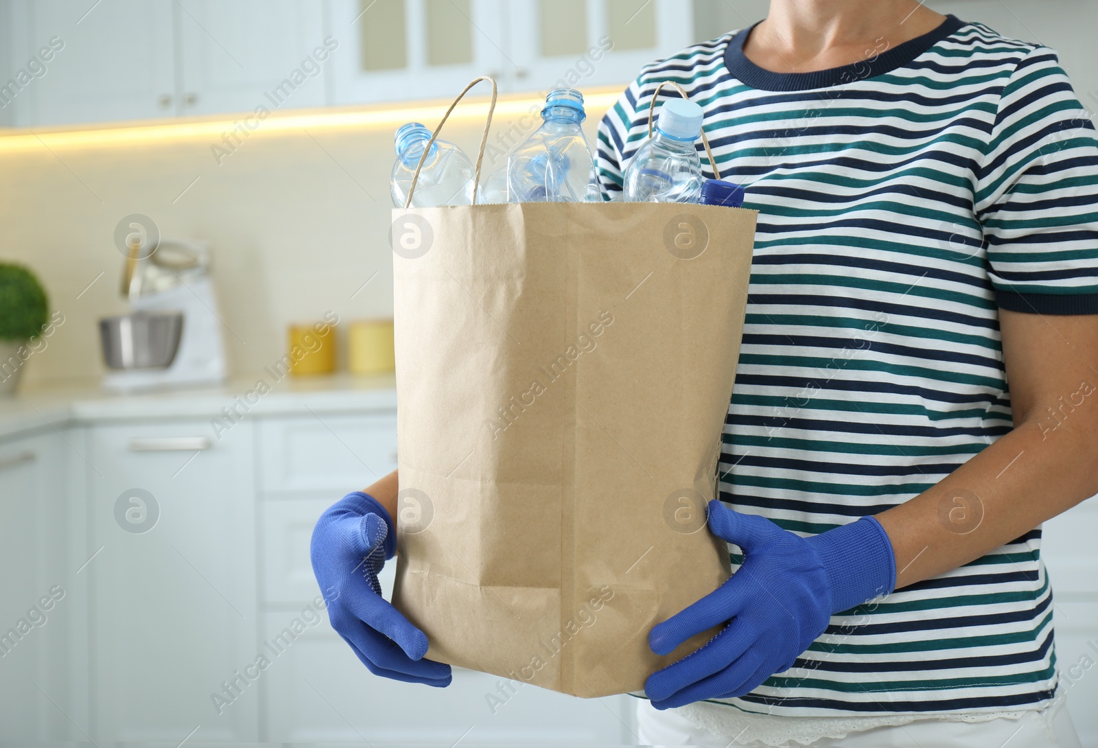 Photo of Woman holding paper bag with used plastic bottles indoors, closeup. Recycling problem