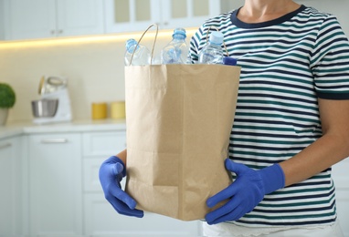 Woman holding paper bag with used plastic bottles indoors, closeup. Recycling problem