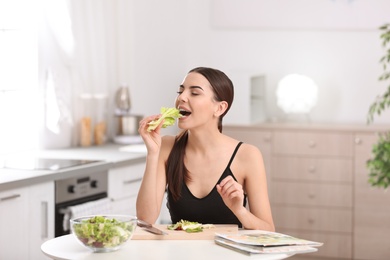 Young woman in fitness clothes eating lettuce while preparing healthy breakfast at home