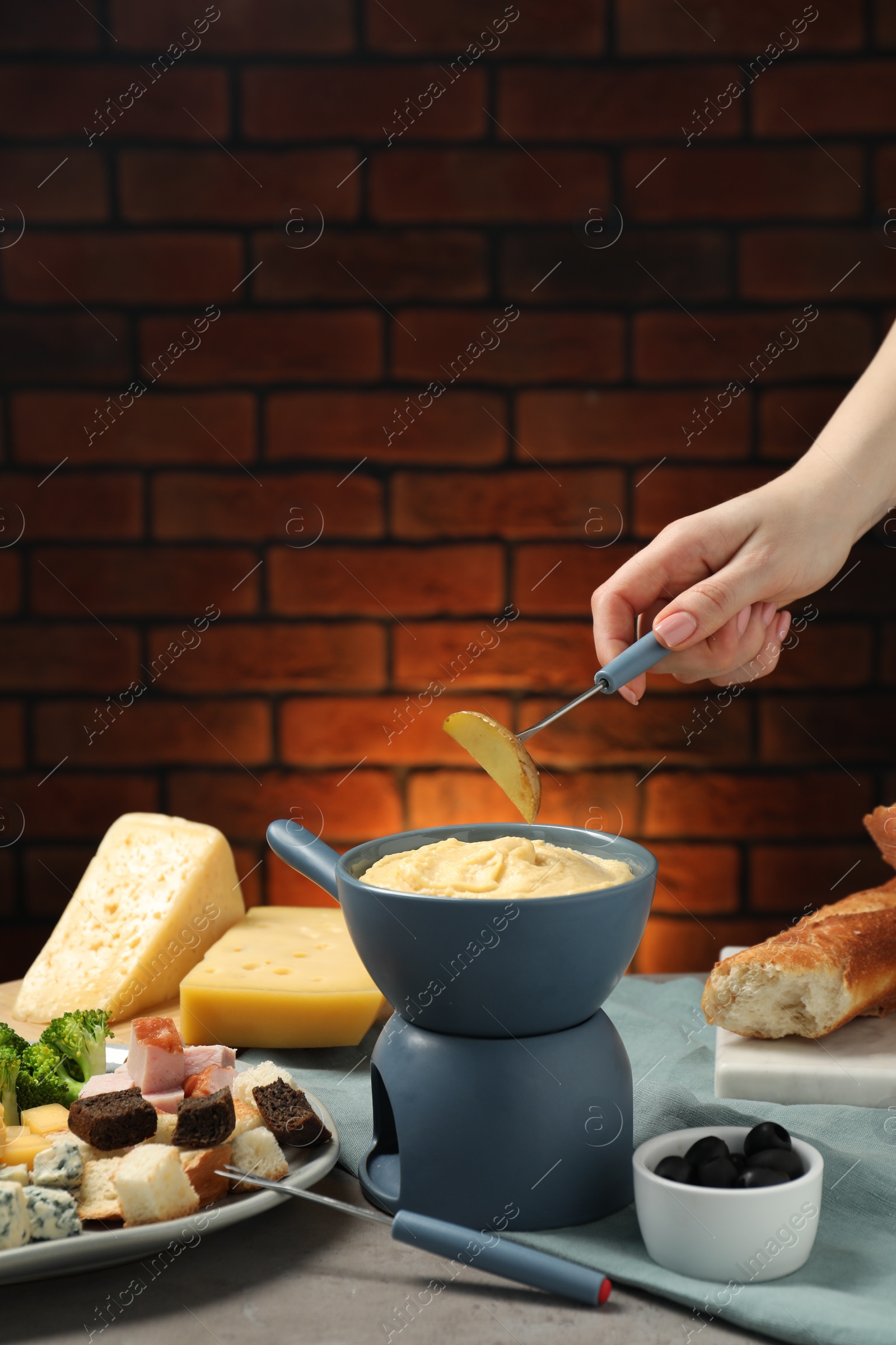 Photo of Woman dipping piece of potato into fondue pot with melted cheese at table with snacks, closeup