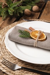 Photo of Festive place setting with beautiful dishware, fabric napkin and dried orange slice for Christmas dinner on wooden table