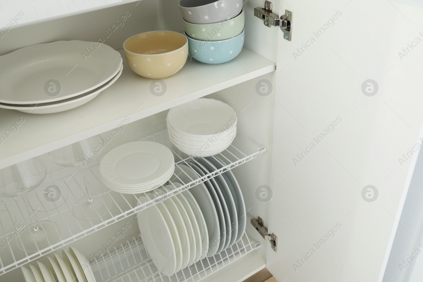 Photo of Clean plates, bowls and glasses on shelves in cabinet indoors