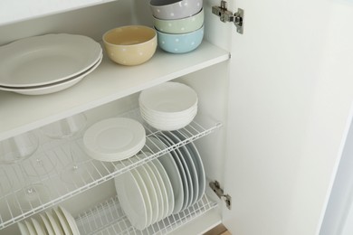 Clean plates, bowls and glasses on shelves in cabinet indoors