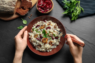 Photo of Woman eating delicious rice pilaf at black table, top view