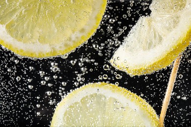 Photo of Juicy lemon slices in soda water against black background, closeup