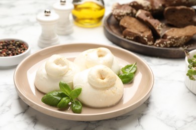 Photo of Delicious burrata cheese with basil on white marble table