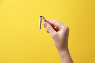 Photo of Stop smoking. Woman holding broken cigarette on yellow background, closeup. Space for text