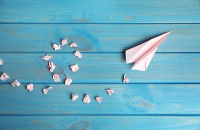 Photo of Handmade plane and many crumpled pieces of paper on light blue wooden table, flat lay