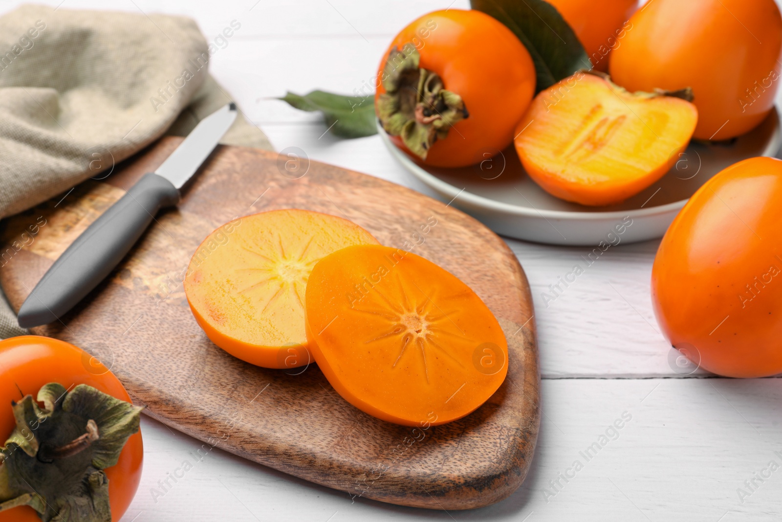 Photo of Delicious ripe juicy persimmons and knife on white wooden table, closeup