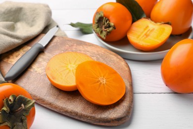 Photo of Delicious ripe juicy persimmons and knife on white wooden table, closeup