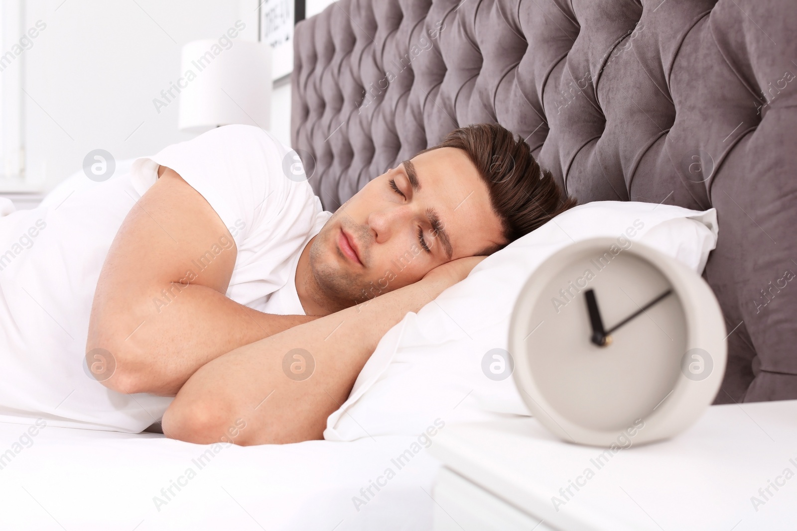 Photo of Young man sleeping in bed and alarm clock on nightstand at home