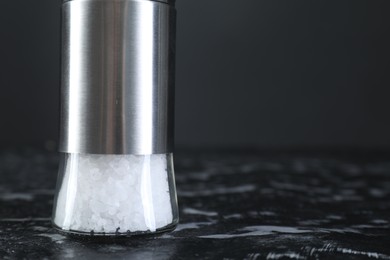 Photo of Salt shaker on dark marble table, closeup. Space for text