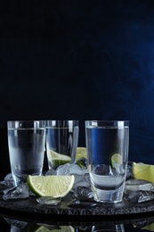 Vodka in shot glasses and lime slices on dark background