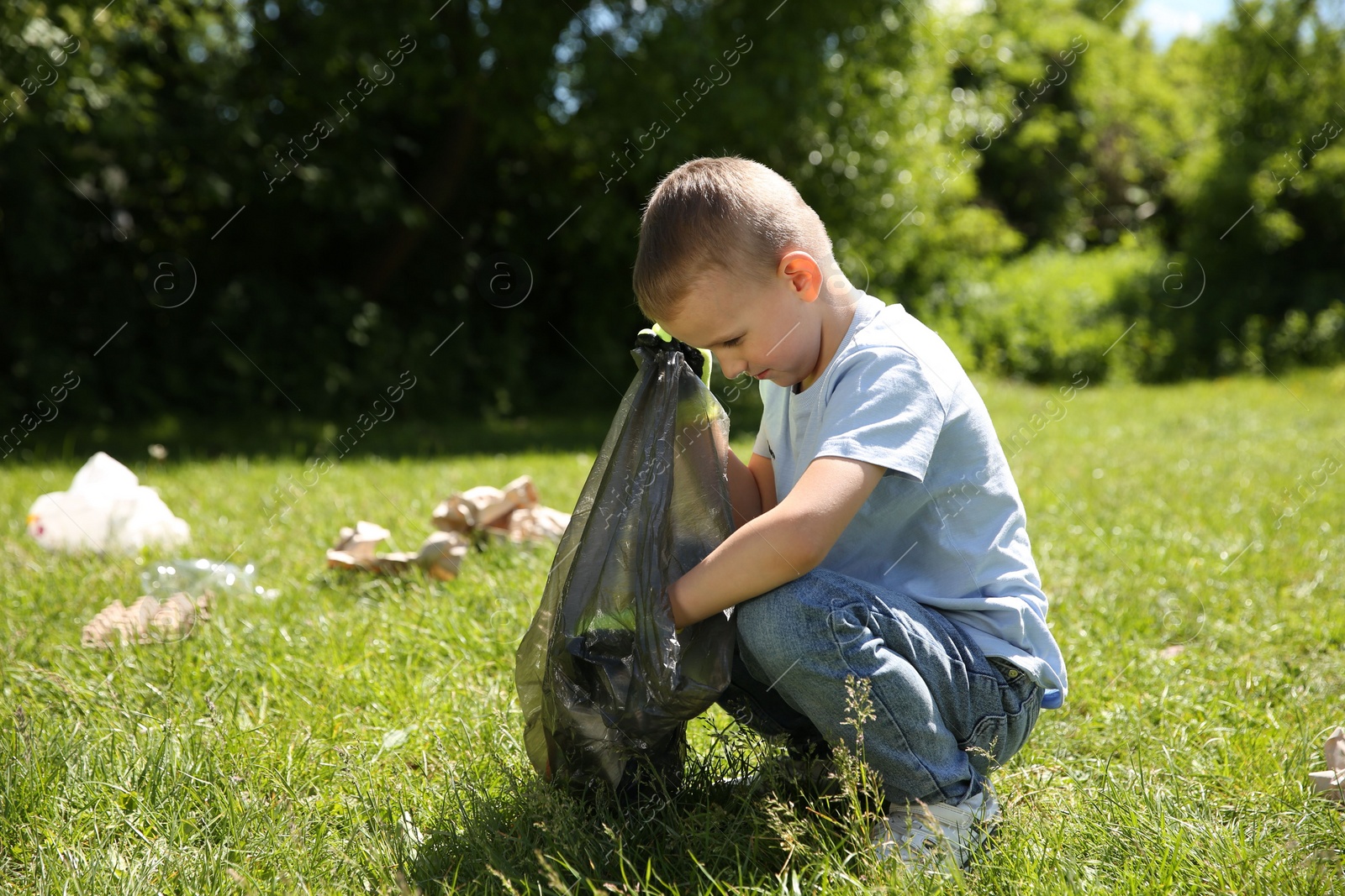 Photo of Little boy with plastic bag collecting garbage in park