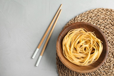 Plate of uncooked egg noodles and chopsticks on grey table, flat lay with space for text