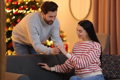 Photo of Making proposal. Man putting engagement ring on his girlfriend's finger at home on Christmas