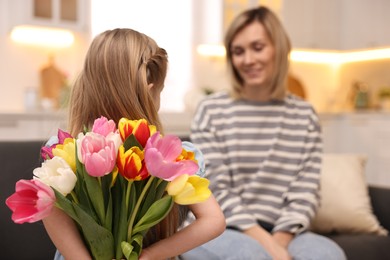 Little girl hiding bouquet of tulips for mom at home, selective focus. Happy Mother's Day