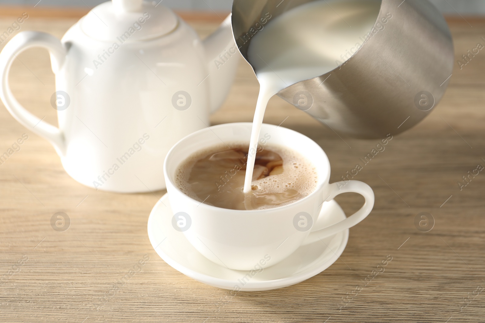 Photo of Pouring milk in tea at wooden table, closeup