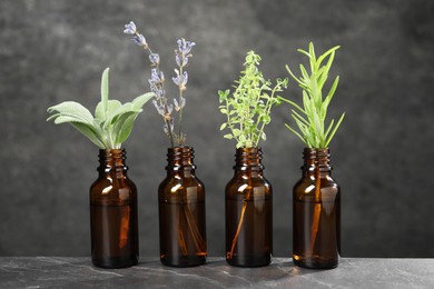 Bottles with essential oils and plants on grey textured table