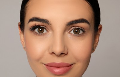 Photo of Beautiful young woman showing extended and ordinary eyelashes on grey background, closeup