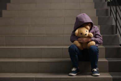 Photo of Child abuse. Upset boy with teddy bear sitting on stairs, space for text