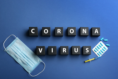 Wooden cubes with words CORONA VIRUS and medicine on blue background, flat lay