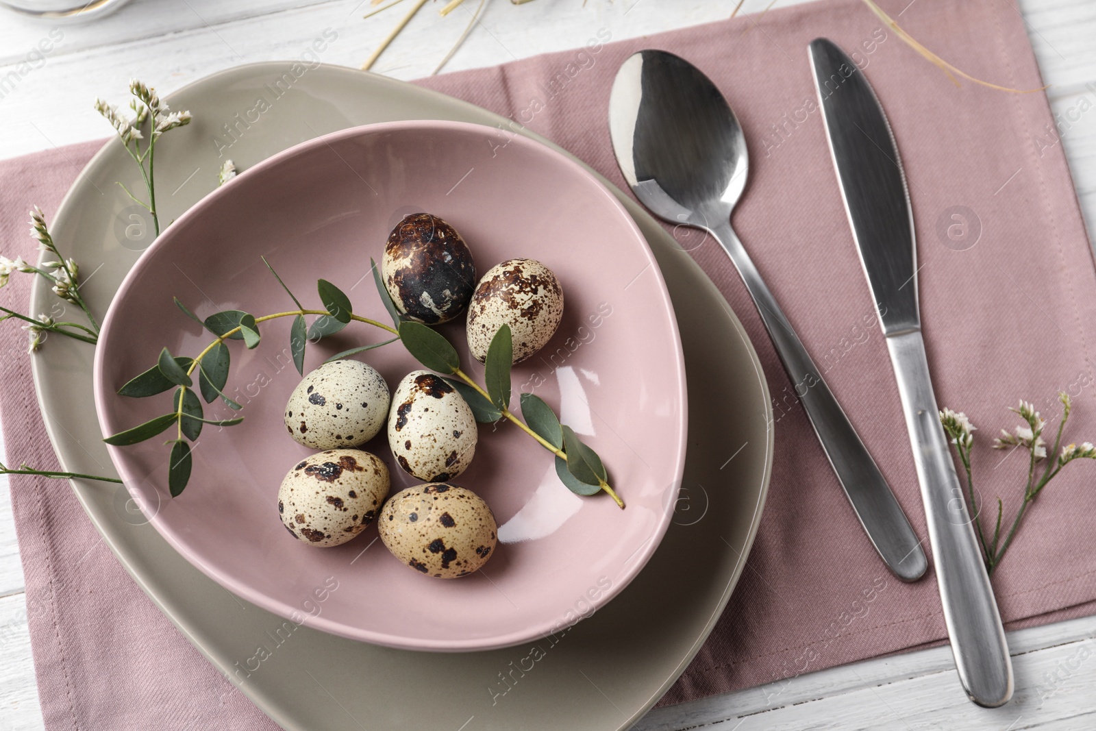 Photo of Festive Easter table setting with quail eggs and floral decoration on wooden background, flat lay