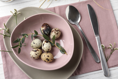 Festive Easter table setting with quail eggs and floral decoration on wooden background, flat lay