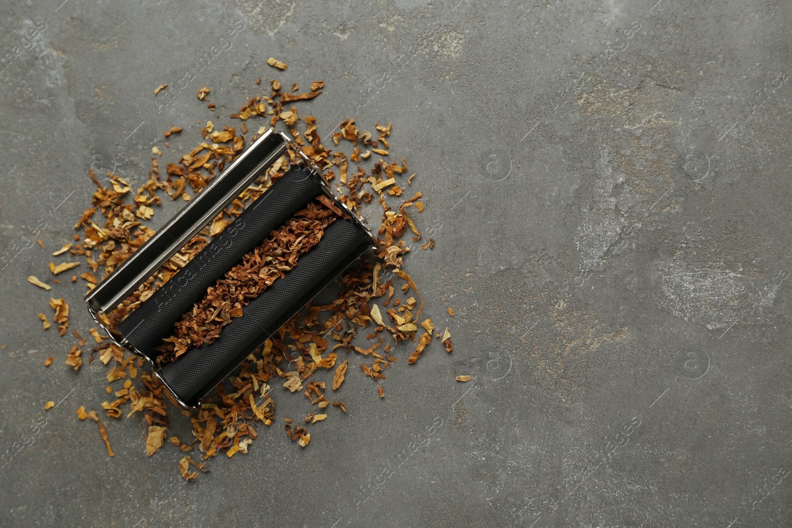 Photo of Roller with tobacco on dark grey table, top view and space for text. Making hand rolled cigarette