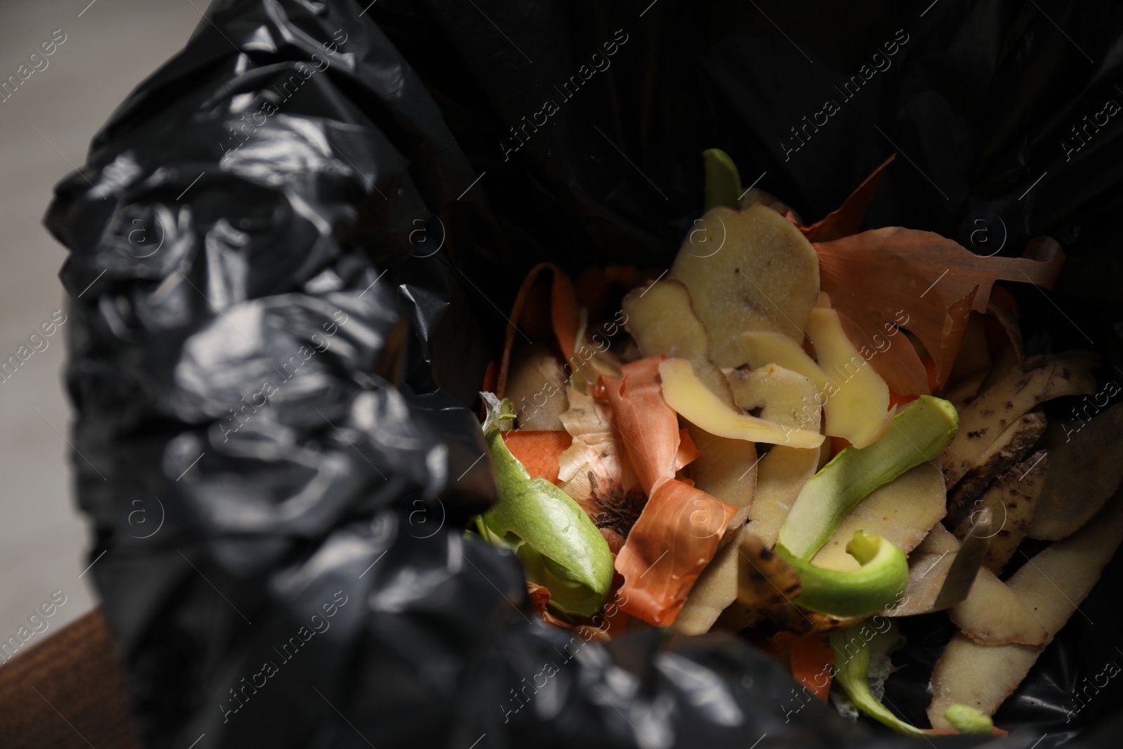 Photo of Garbage bin with peels of fresh vegetables indoors, closeup