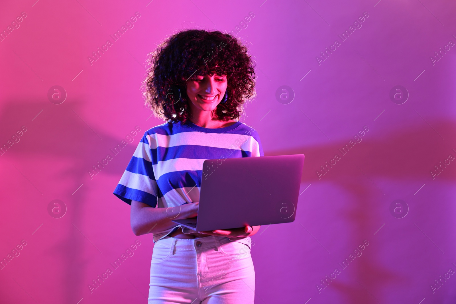 Photo of Beautiful young woman with laptop on color background in neon lights