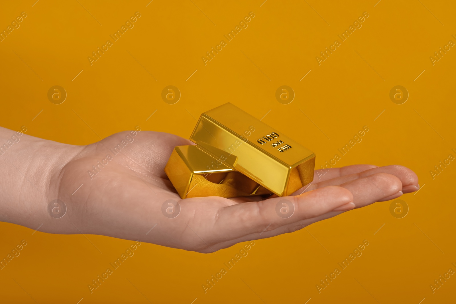 Photo of Woman holding gold bars on orange background, closeup