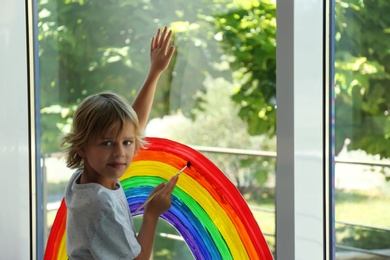 Photo of Little boy drawing rainbow on window. Stay at home concept