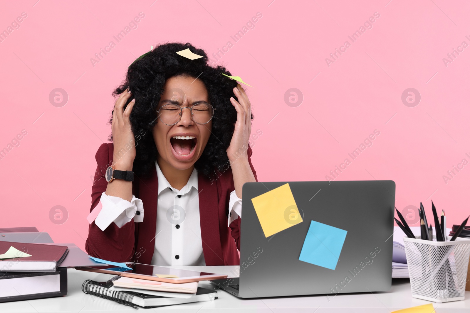 Photo of Stressful deadline. Screaming woman at white table against pink background. Sticky notes everywhere as reminders