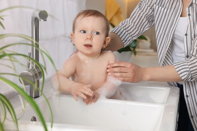 Mother washing her little baby in sink at home