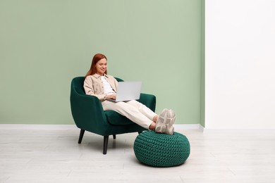 Photo of Happy young woman with laptop relaxing in armchair near light olive wall indoors