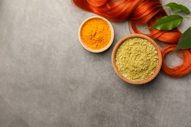 Henna, turmeric powder, red strand and green leaves on grey table, flat lay with space for text. Natural hair coloring