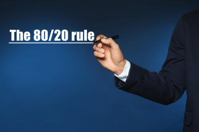 Image of Pareto principle concept. Man writing 80/20 rule on blue background, closeup