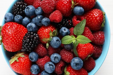 Many different fresh ripe berries in bowl on white wooden table, top view